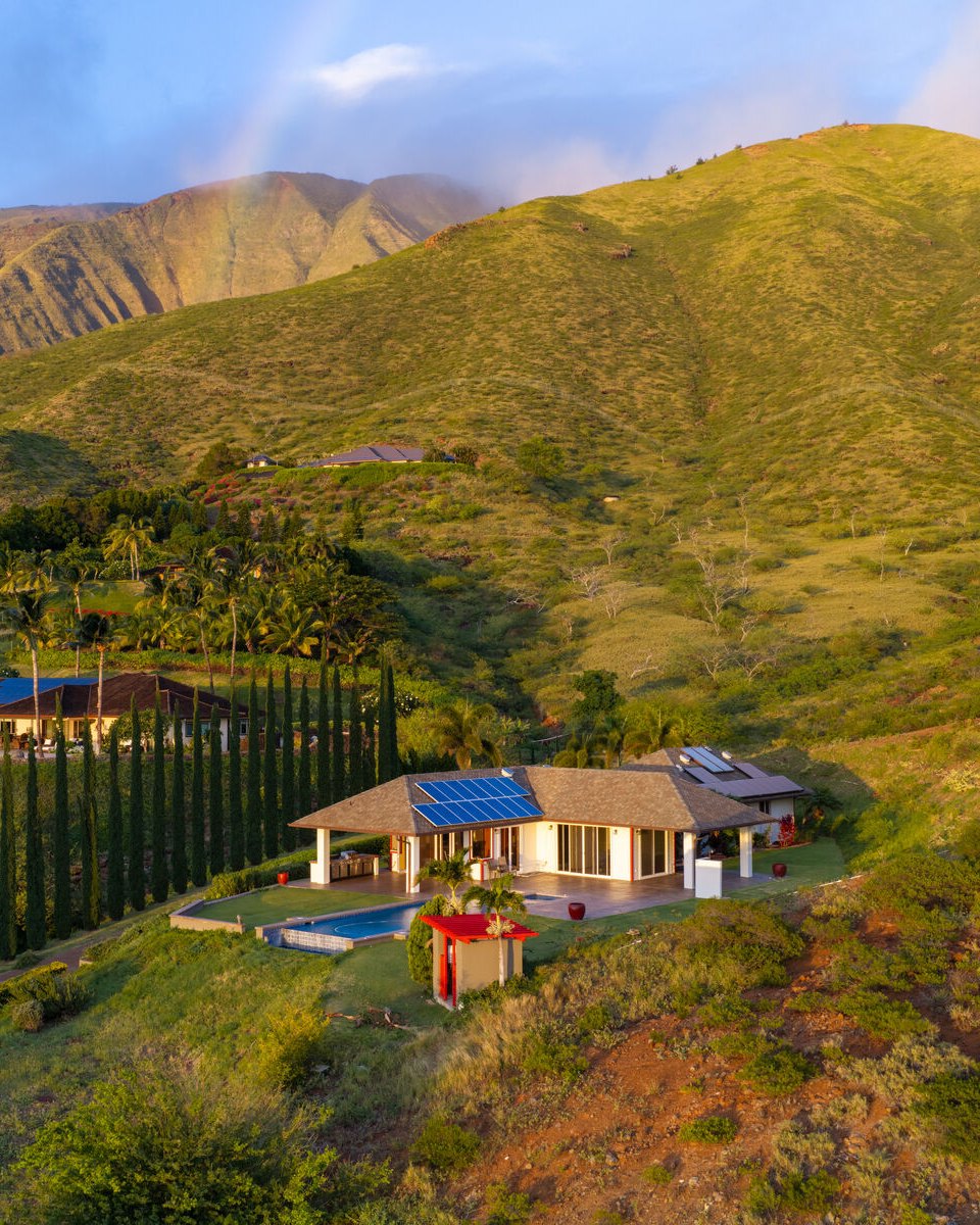 The residence, pool and cypress drive in golden light beneath the West Maui Mountains, with a rainbow over the ridge